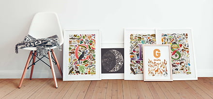 picture of five Renard Roux posters in frames leaned against a white wall next to a chair